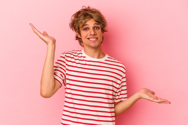 Young caucasian man with make up isolated on pink background confused and doubtful shrugging shoulders to hold a copy space.