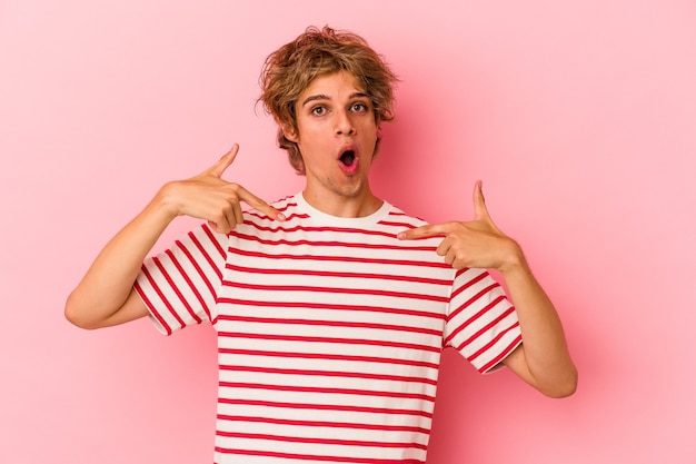 Young caucasian man with make up isolated on pink background points down with fingers, positive feeling.