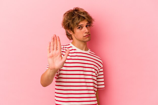 Young caucasian man with make up isolated on pink background rejecting someone showing a gesture of disgust.