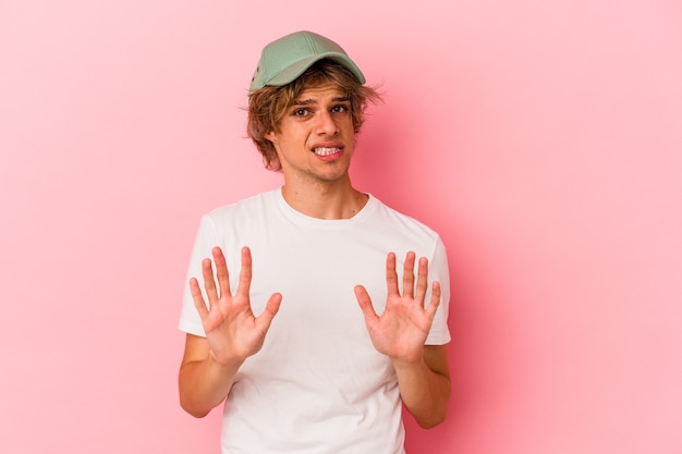 Young caucasian man with make up isolated on pink background rejecting someone showing a gesture of disgust.