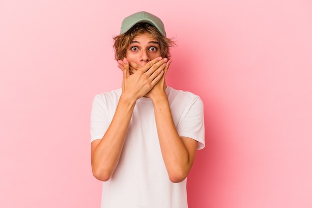 Young caucasian man with make up isolated on pink background shocked covering mouth with hands.