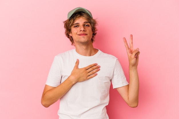 Young caucasian man with make up isolated on pink background taking an oath, putting hand on chest.