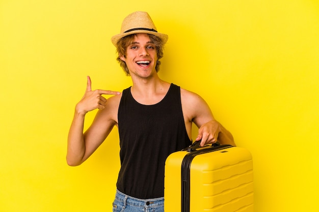 Young caucasian man with makeup going to travel isolated on yellow background  person pointing by hand to a shirt copy space, proud and confident
