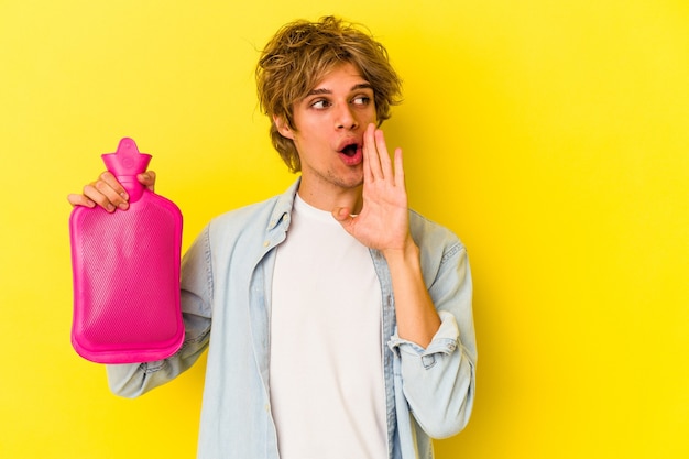 Young caucasian man with makeup holding a hot bag of water\
isolated on yellow background is saying a secret hot braking news\
and looking aside