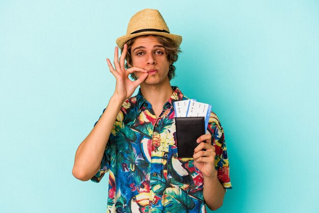Young caucasian man with makeup holding passport isolated on blue background  with fingers on lips keeping a secret.