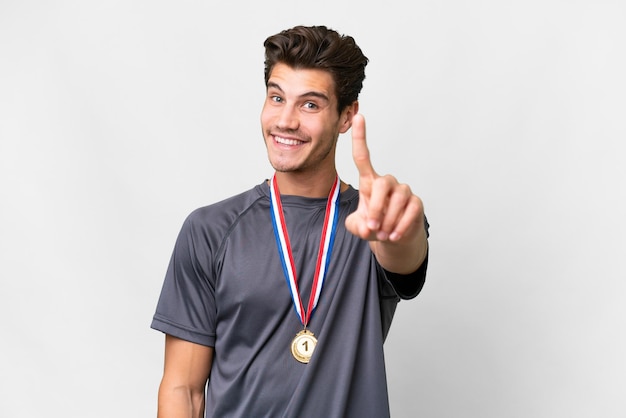Young caucasian man with medals over isolated white background showing and lifting a finger