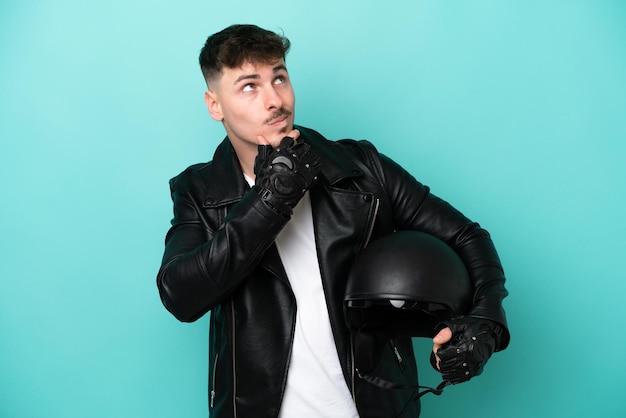 Молодой кавказец в мотоциклетном шлеме на синем фоне сомневается