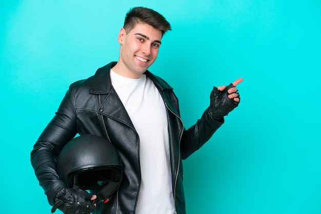 Young caucasian man with a motorcycle helmet isolated on blue background pointing finger to the side