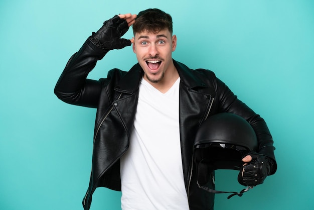 Young caucasian man with a motorcycle helmet isolated on blue background with surprise expression