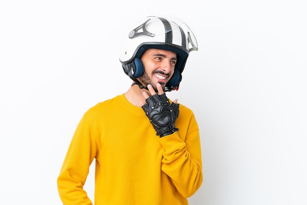 Young caucasian man with a motorcycle helmet isolated on white background looking up while smiling