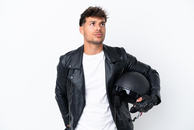 Young caucasian man with a motorcycle helmet isolated on white background and looking up