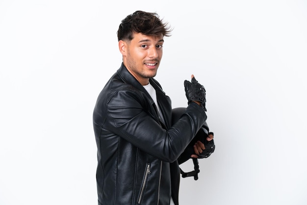 Young caucasian man with a motorcycle helmet isolated on white background pointing back