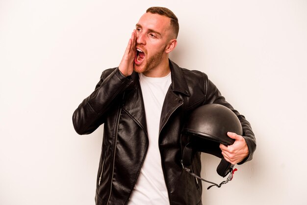 Young caucasian man with a motorcycle helmet isolated on white background shouting and holding palm near opened mouth