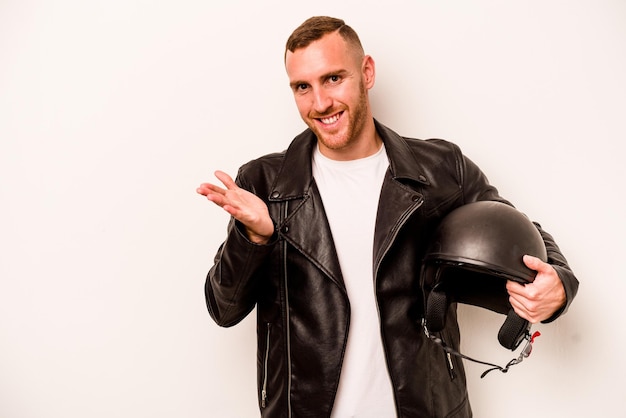 Young caucasian man with a motorcycle helmet isolated on white background showing a copy space on a palm and holding another hand on waist