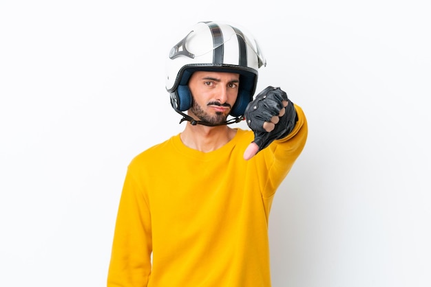 흰색 배경에 격리된 오토바이 헬멧을 쓴 백인 청년이 부정적인 표정으로 엄지손가락을 아래로 내리고 있다