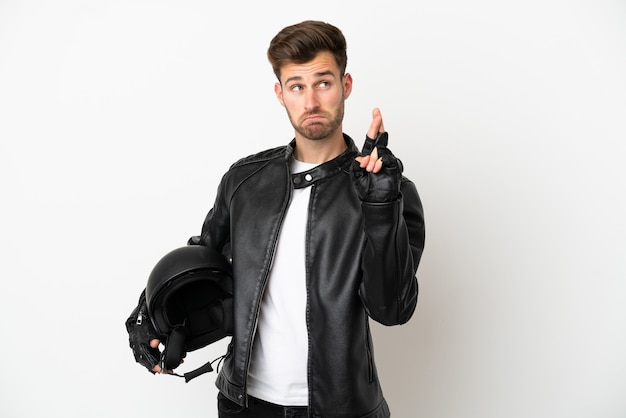 Young caucasian man with a motorcycle helmet isolated on white background with fingers crossing and wishing the best