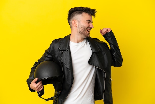 勝利を祝う黄色の背景に分離されたオートバイのヘルメットを持つ若い白人男性