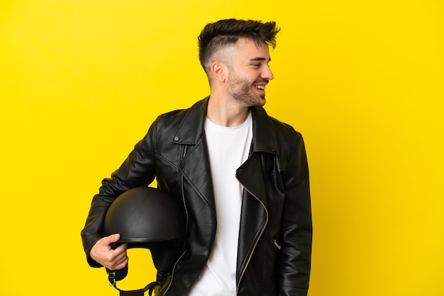 Young caucasian man with a motorcycle helmet isolated on yellow background looking side