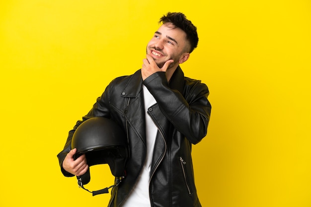 노란색 배경에 오토바이 헬멧을 쓴 백인 청년이 웃고 있는 동안 올려다보고 있다
