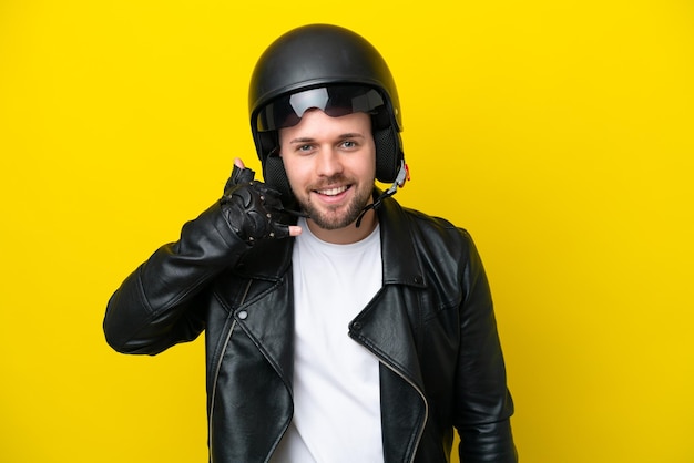 Young caucasian man with a motorcycle helmet isolated on yellow background making phone gesture Call me back sign