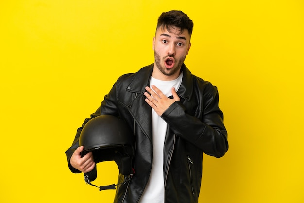 Giovane uomo caucasico con un casco da motociclista isolato su sfondo giallo sorpreso e scioccato mentre guardava a destra