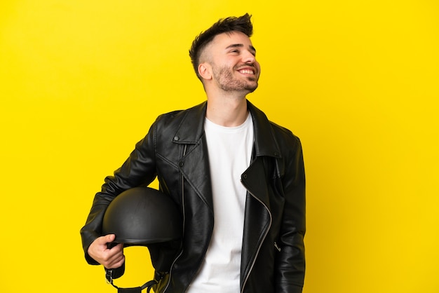 Young caucasian man with a motorcycle helmet isolated on yellow background thinking an idea while looking up