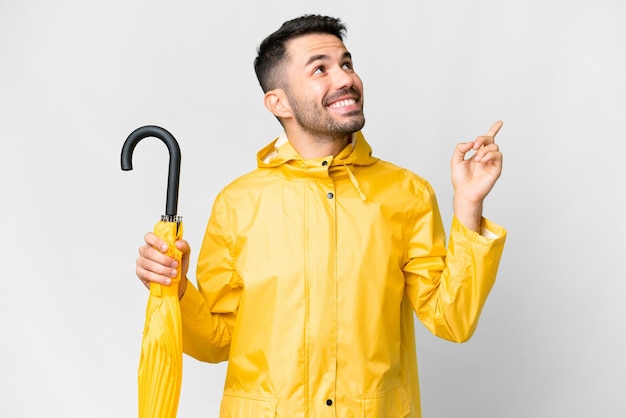 防雨コートと素晴らしいアイデアを指している分離の白い背景の上に傘を持つ若い白人男性