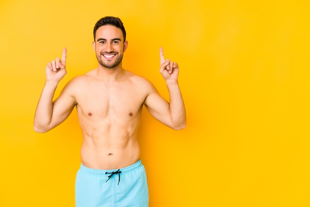 Young caucasian man with swimsuit isolated on yellow