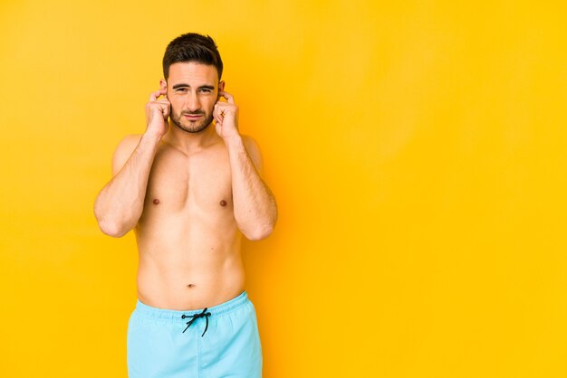 Young caucasian man with swimsuit isolated on yellow