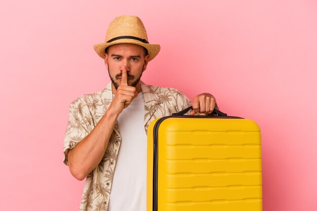 Young caucasian man with tattoos going to travel isolated on pink background  keeping a secret or asking for silence.