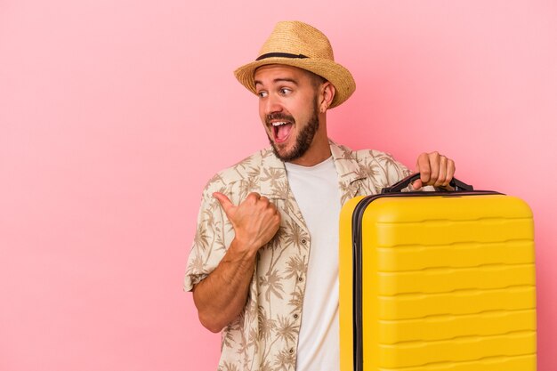 Young caucasian man with tattoos going to travel isolated on pink background  points with thumb finger away, laughing and carefree.