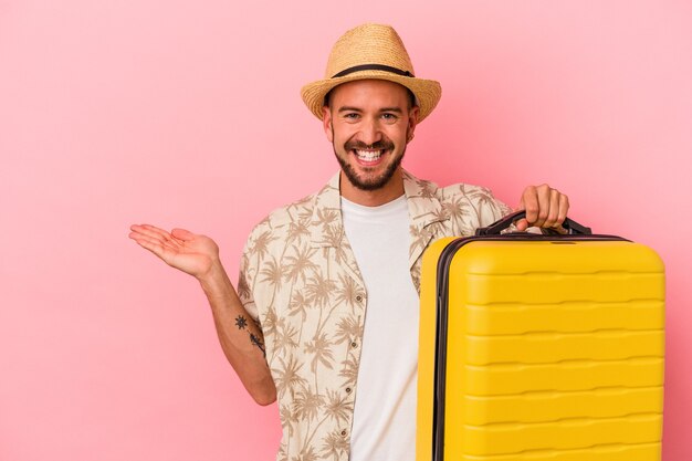 Young caucasian man with tattoos going to travel isolated on pink background  showing a copy space on a palm and holding another hand on waist.