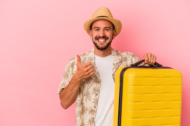 Young caucasian man with tattoos going to travel isolated on pink background  smiling and raising thumb up