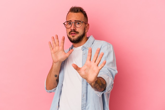 Young caucasian man with tattoos isolated on pink background  being shocked due to an imminent danger