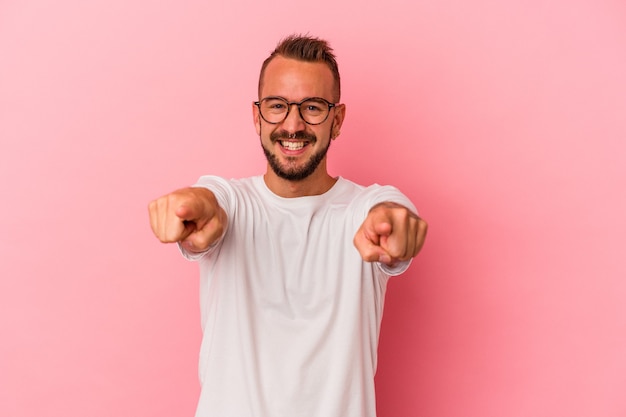 Young caucasian man with tattoos isolated on pink background  cheerful smiles pointing to front.