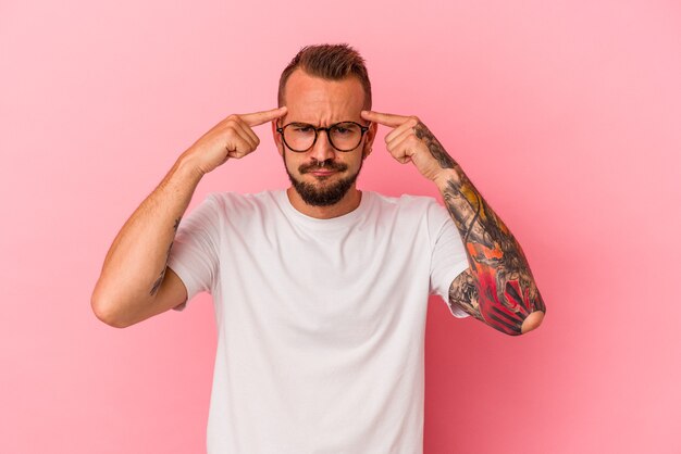 Photo young caucasian man with tattoos isolated on pink background  focused on a task, keeping forefingers pointing head.