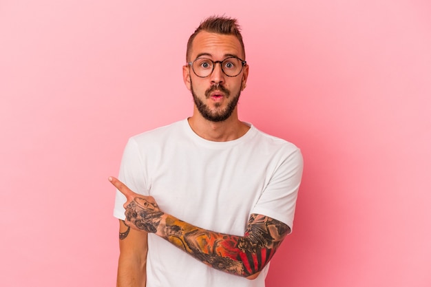 Foto giovane uomo caucasico con tatuaggi isolati su sfondo rosa che puntano al lato
