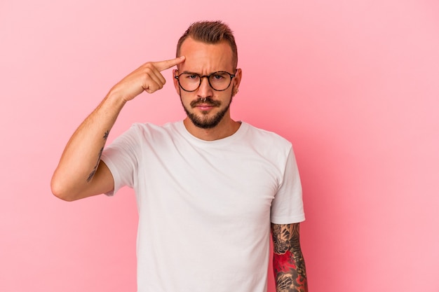 Young caucasian man with tattoos isolated on pink background  pointing temple with finger, thinking, focused on a task.