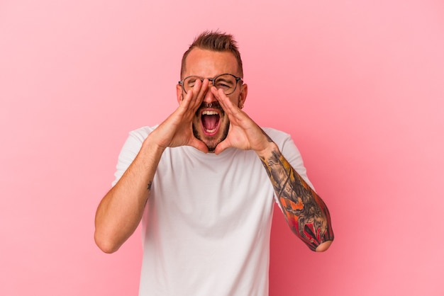 Young caucasian man with tattoos isolated on pink background  shouting excited to front.