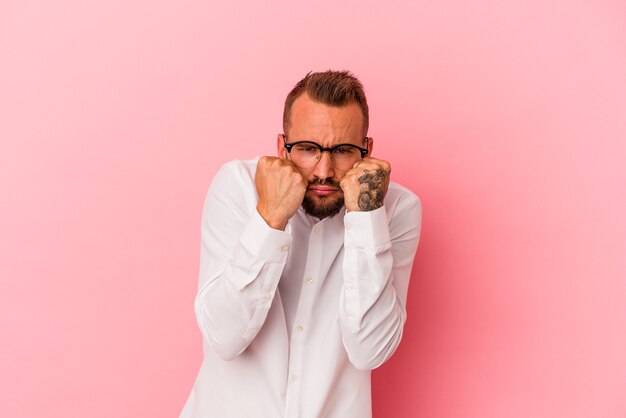 Young caucasian man with tattoos isolated on pink background  throwing a punch, anger, fighting due to an argument, boxing.