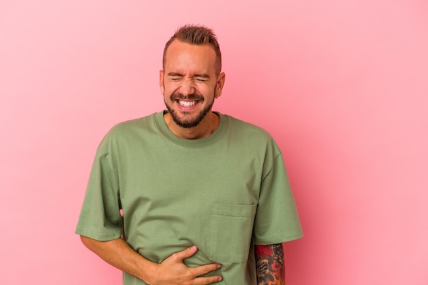 Young caucasian man with tattoos isolated on pink background  touches tummy, smiles gently, eating and satisfaction concept.