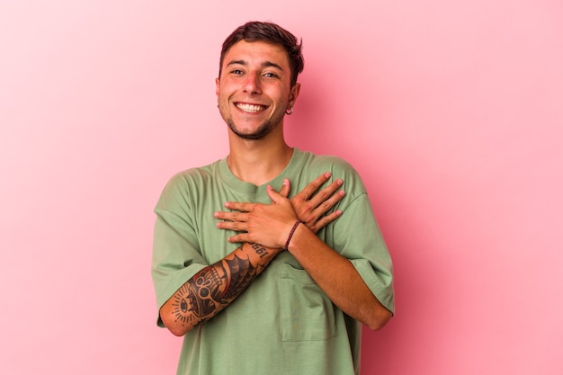 Young caucasian man with tattoos isolated on yellow background  has friendly expression, pressing palm to chest. Love concept.