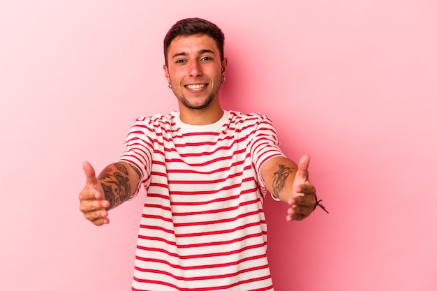 Young caucasian man with tattoos isolated on yellow background  showing a welcome expression.