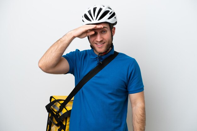young caucasian man with thermal backpack isolated on white background looking far away with hand to look something
