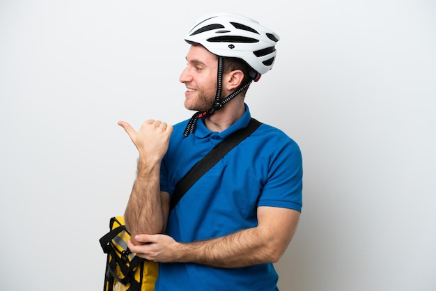 Young caucasian man with thermal backpack isolated on white background pointing to the side to present a product