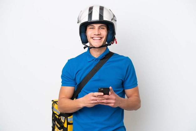 モバイルでメッセージを送信する白い背景で隔離のサーマルバックパックを持つ若い白人男性