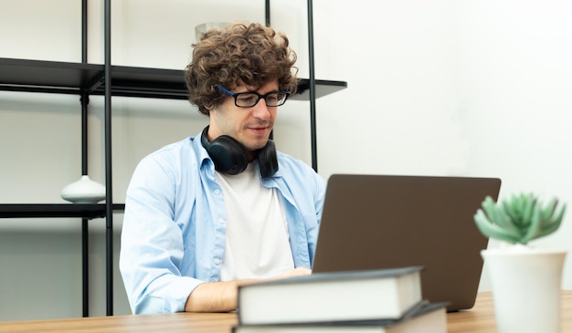 Il giovane uomo caucasico lavora da casa sul laptop e si connette online all'ufficio al chiuso per il posto di lavoro internet remoto