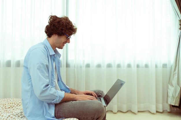 Il giovane uomo caucasico lavora da casa sul laptop e si connette online all'ufficio al chiuso per il posto di lavoro internet remoto