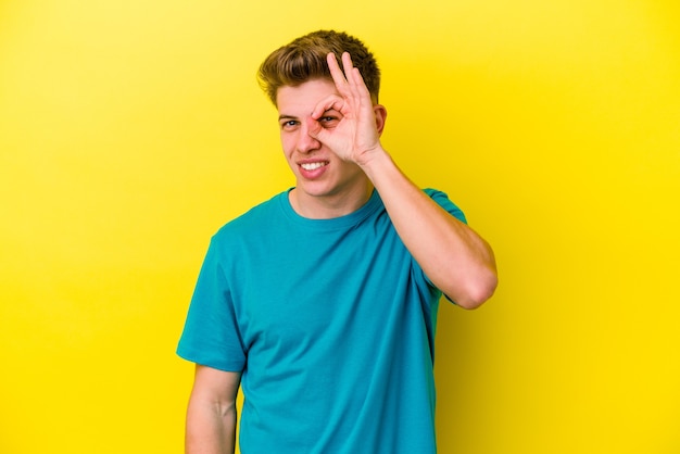 Young caucasian man on yellow excited keeping ok gesture on eye.