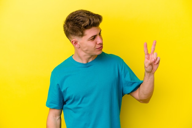 Young caucasian man on yellow joyful and carefree showing a peace symbol with fingers.